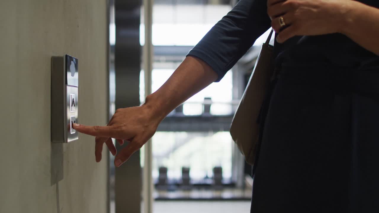 Midsection of caucasian businesswoman pressing button in lift arriving in modern office
