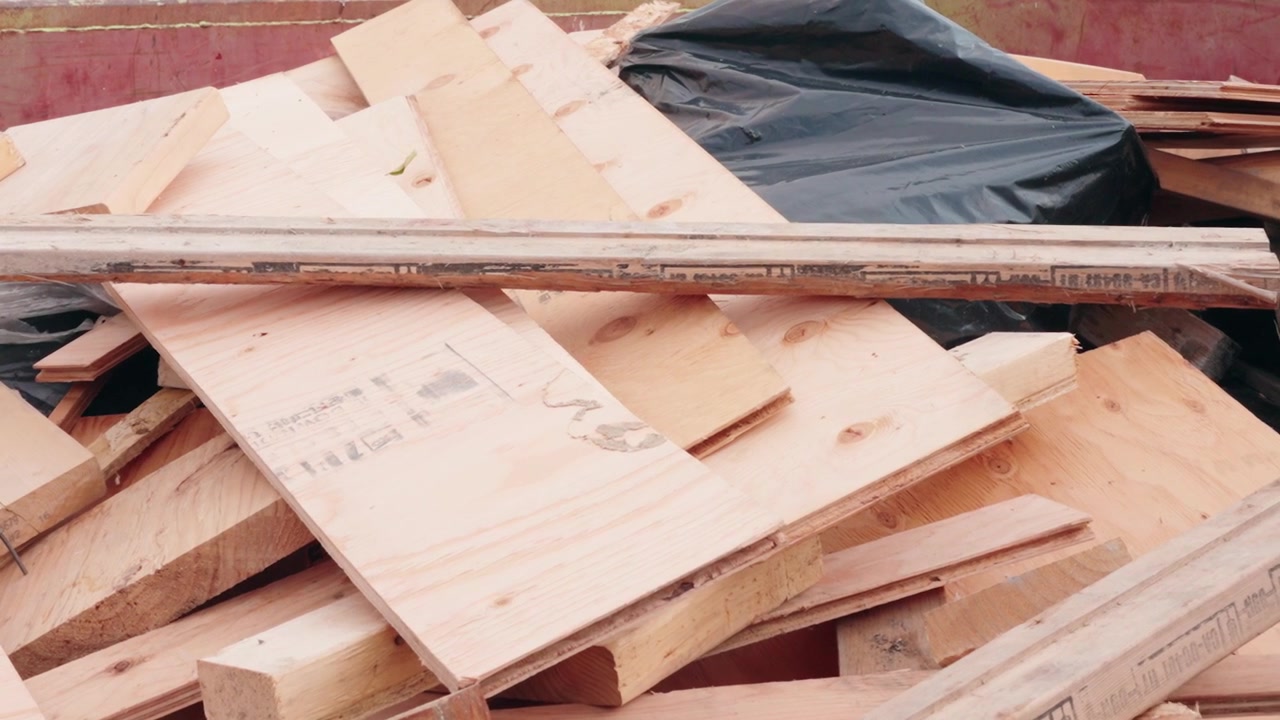 Inquadratura panoramica ravvicinata di un cassone per rifiuti edili mentre legname di scarto viene gettato su un mucchio di detriti durante la pulizia in un cantiere residenziale attivo