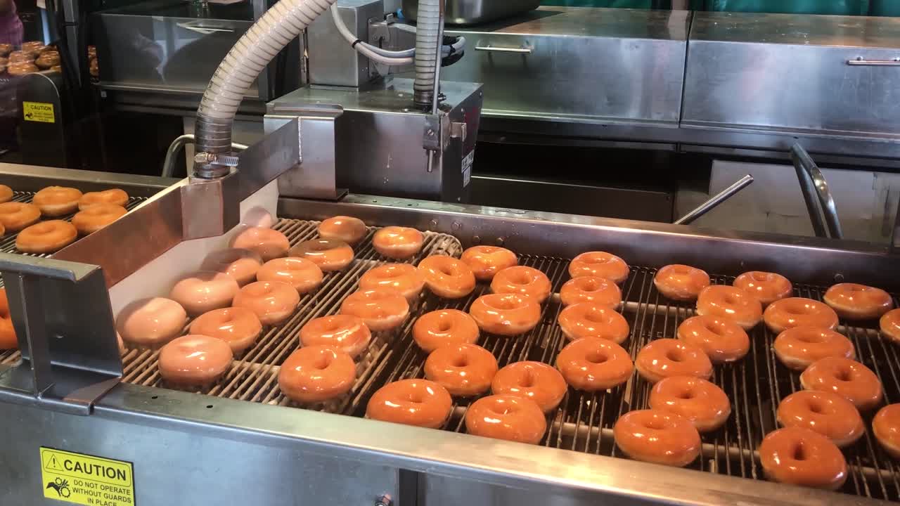 The decadent and gorgeous sugar glazing process of ring doughnuts as they pass through a continuous wall of liquid sugar glaze