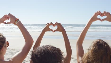grupo de amigos haciendo un gesto en forma de corazón con sus manos en la playa