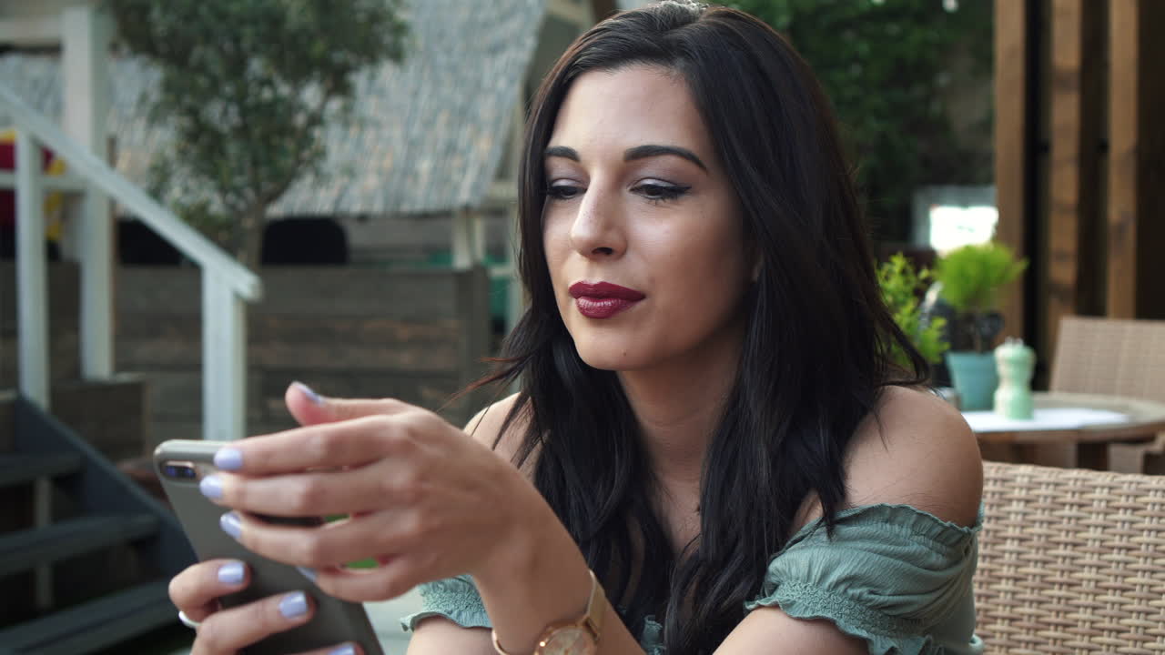 joven morena segura y atractiva con un top informal, usa su teléfono celular, sonríe alegremente a los mensajes de texto, mira a su alrededor