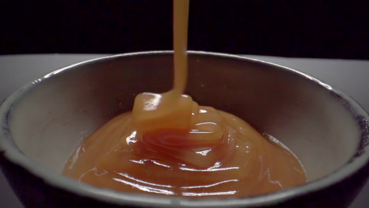 Close up shot of honey falling into a bowl against a black background. Slow motion