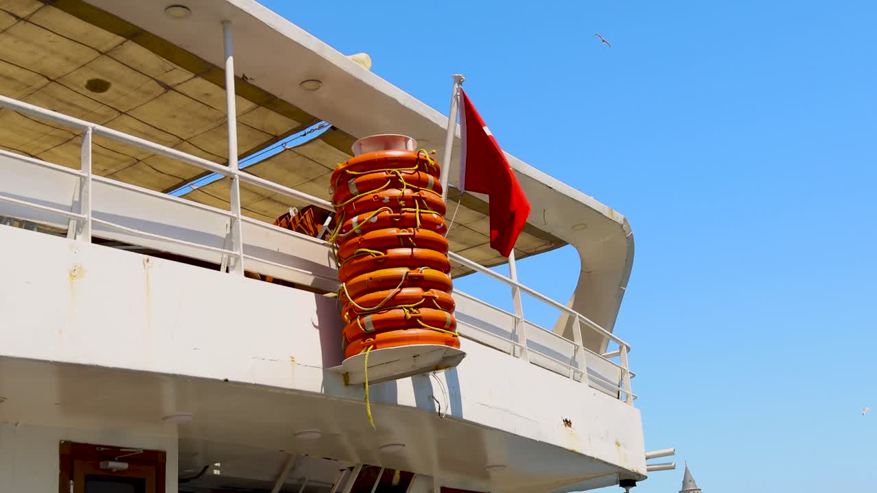 Turkish flag waving on ferry beside bright red life preservers under clear blue sky