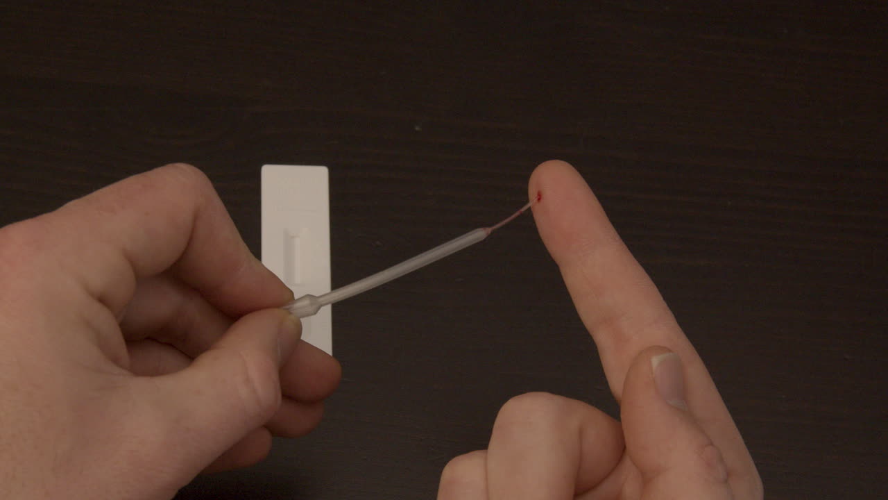 pipette sucking up drop of blood from finger in preparation of Covid-19 self test