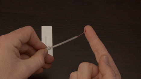 pipette sucking up drop of blood from finger in preparation of Covid-19 self test