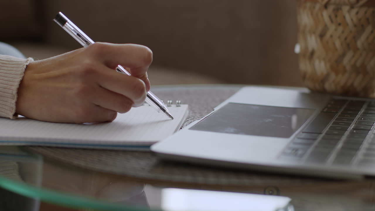 Woman taking notes on a notepad with a pen next to a laptop