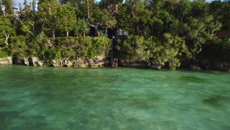 a woman sits on stairs to the lagoon and waves goodbye - pull back aerial view of the paradisiacal location on the isle of pines