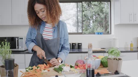 biracial woman wearing apron preparing meal, chopping vegetables in kitchen, slow motion