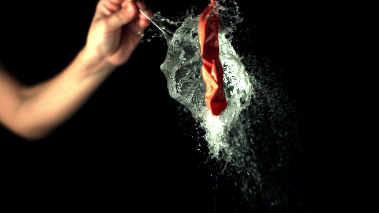 Palloncino d'Acqua Rosso Che Esplode al Rallentatore su Sfondo Nero.