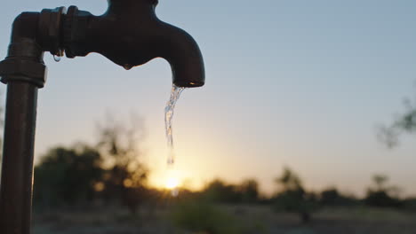 Agua-Del-Grifo-Que-Fluye-En-Una-Granja-Rural-Al-Atardecer-Agua-Dulce-Saliendo-Del-Grifo-Al-Aire-Libre-Desperdiciando-Escasez-De-Agua-En-Las-Tierras-De-Cultivo-Sequía