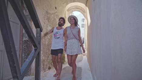 Una-Pareja-Joven-Cogida-De-La-Mano-Da-Un-Paseo-Romántico-Por-Los-Callejones-De-Mykonos,-Grecia