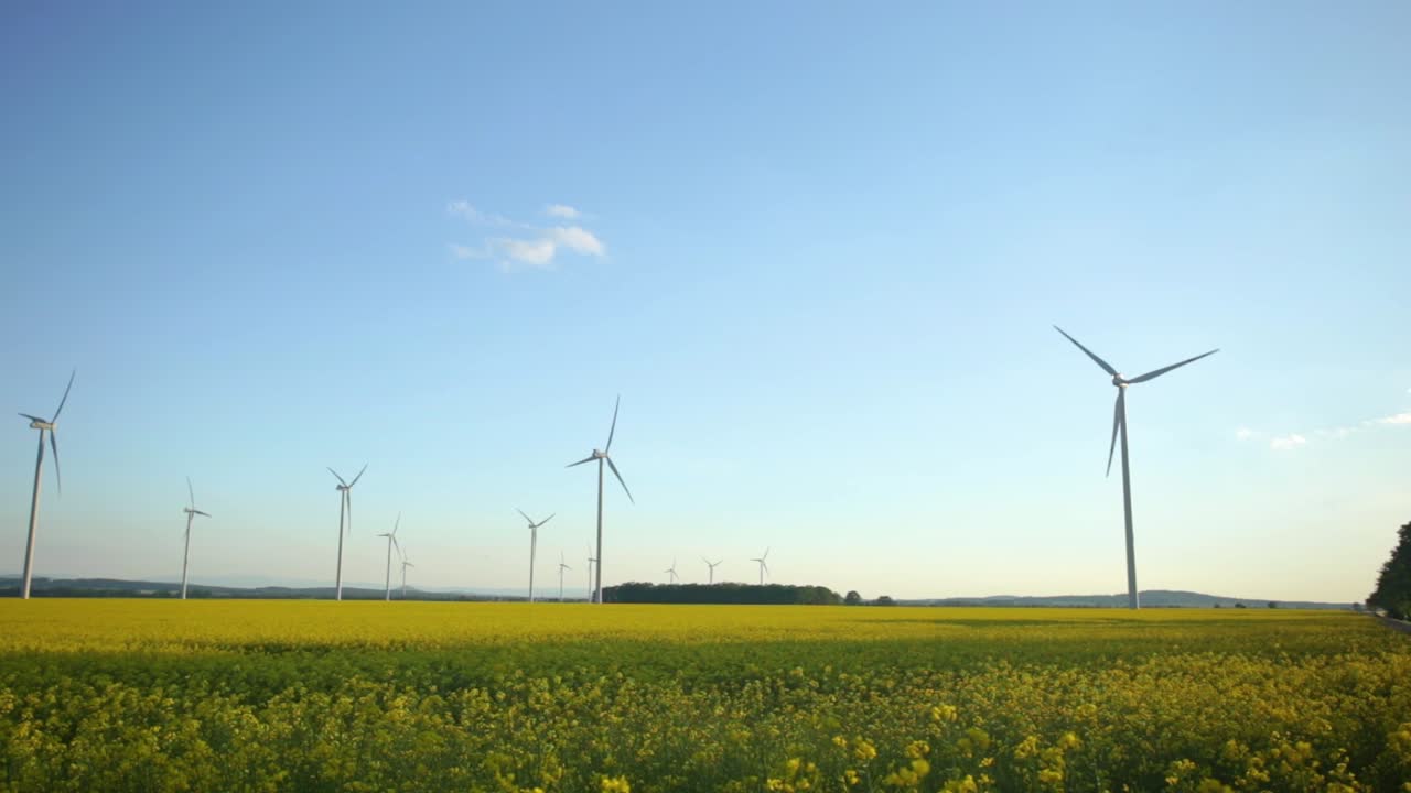 Beautiful white windmills spinning and harvesting wind energy over bright green farmland in Zlotoryja, Poland - wide