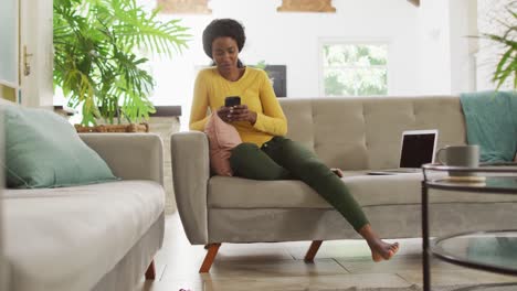 Video-of-happy-african-american-woman-on-sofa-using-smartphone