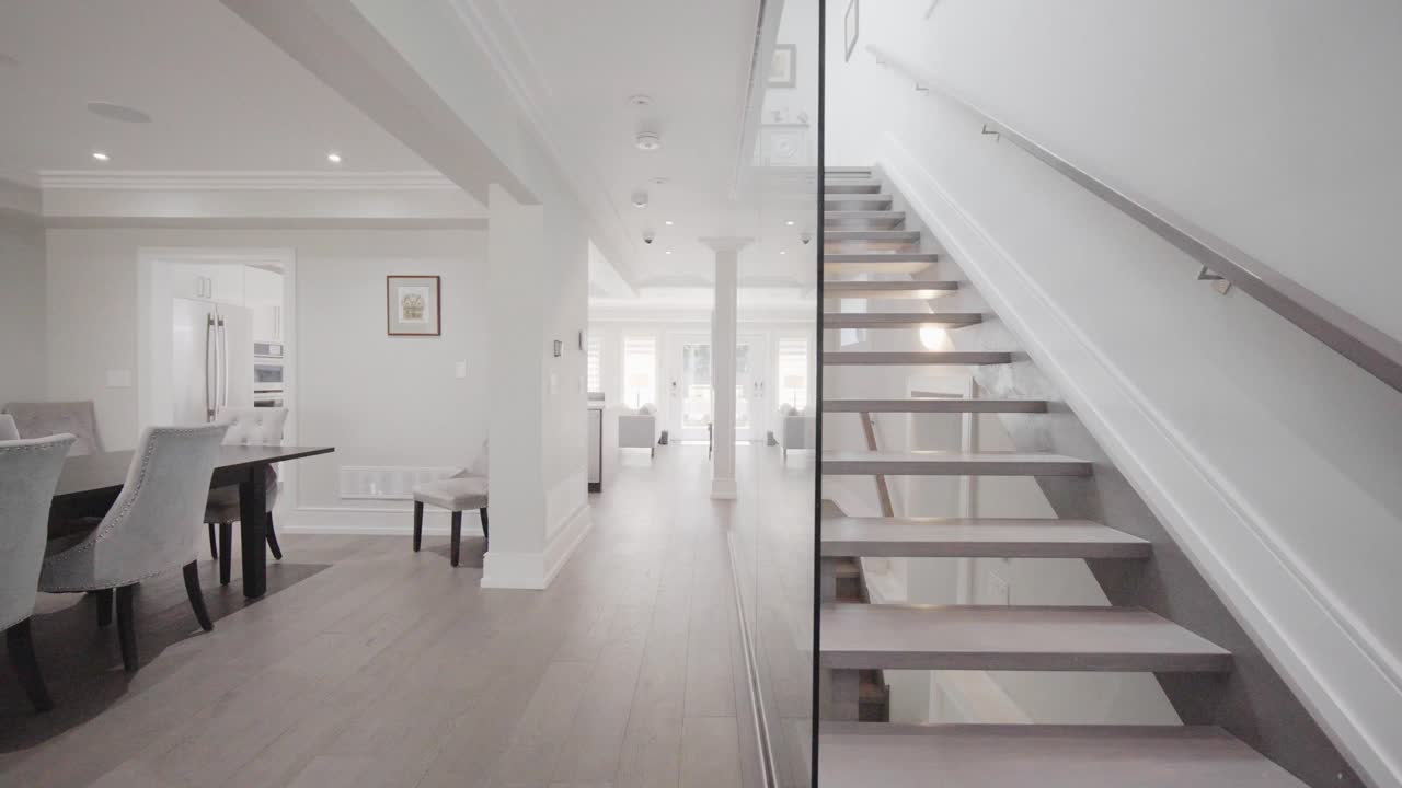 dolly shot desde la escalera transparente a través de la pared de vidrio a la derecha hasta el pasillo con una esquina del comedor a la izquierda en una casa