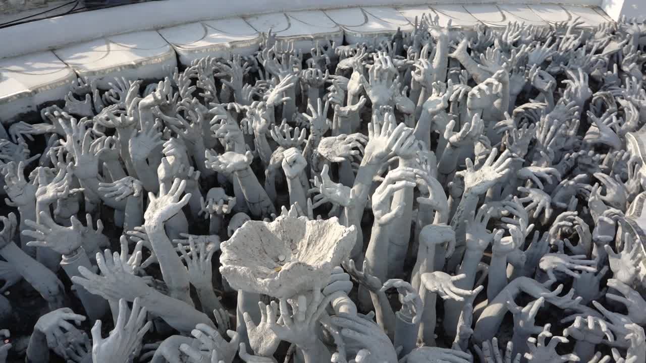 Dozens of hand sculptures rising in the air from the ground at the White Temple, Thailand.