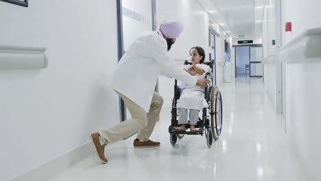 happy biracial doctor walking and talking to sick girl patient in wheelchair in slow motion