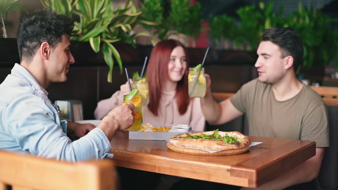 Three young friends opening a soda bottle and playing guitar near a lake in a park