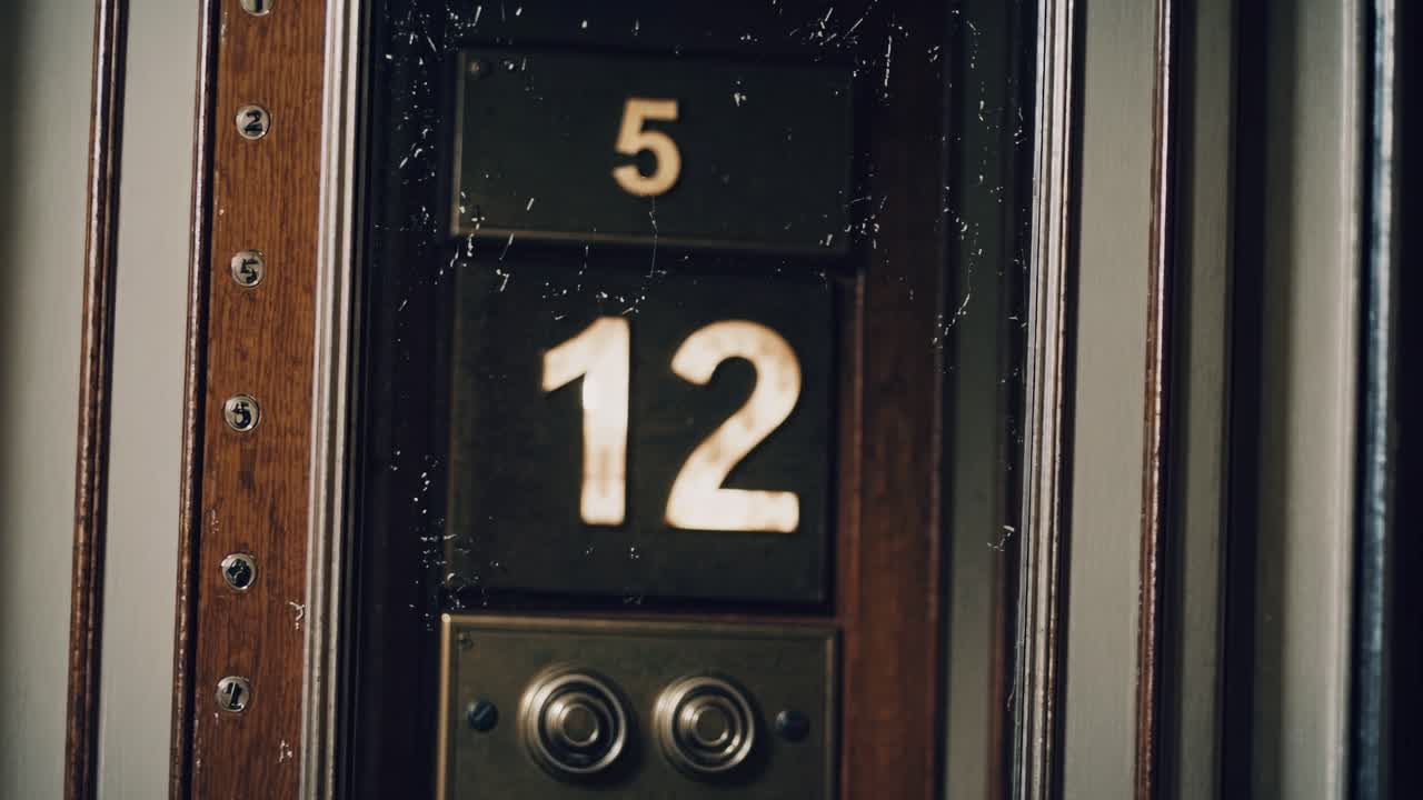 Close up of a vintage elevator indicator displaying the number twelve, with visible floor buttons and a wooden frame, evoking a sense of nostalgia and old fashioned transportation