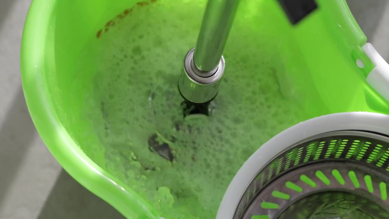 Close-up of a spin mop rotating inside a green bucket, removing excess water and preparing for efficient household floor cleaning.