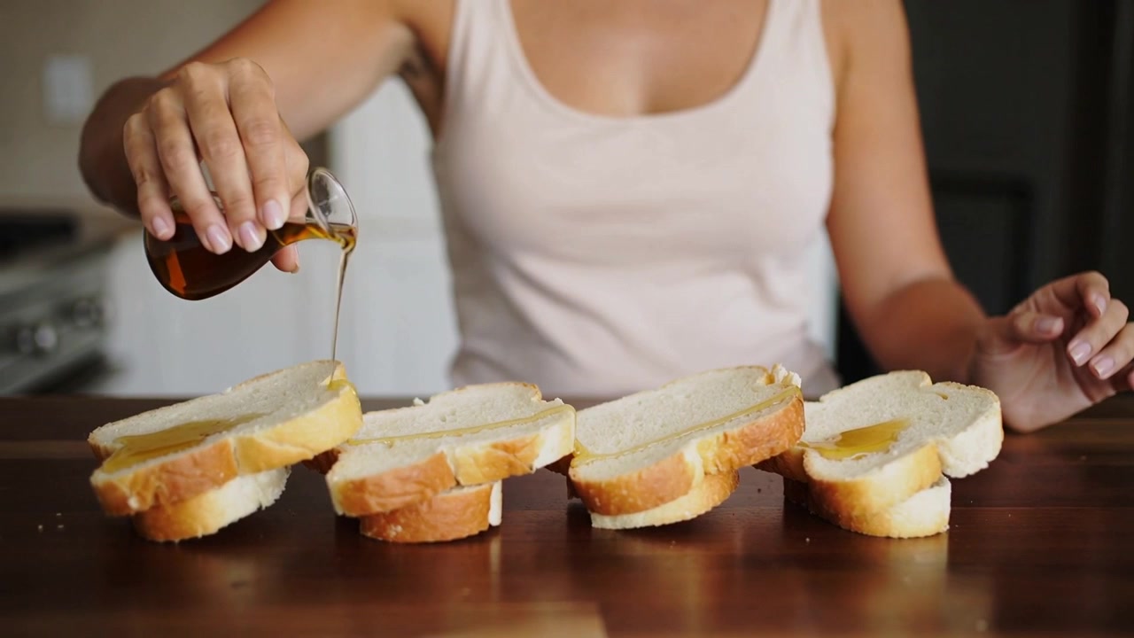Donna in canottiera che allunga la mano verso il dosatore, versando sciroppo su fette di pane in cucina, preparando toast.