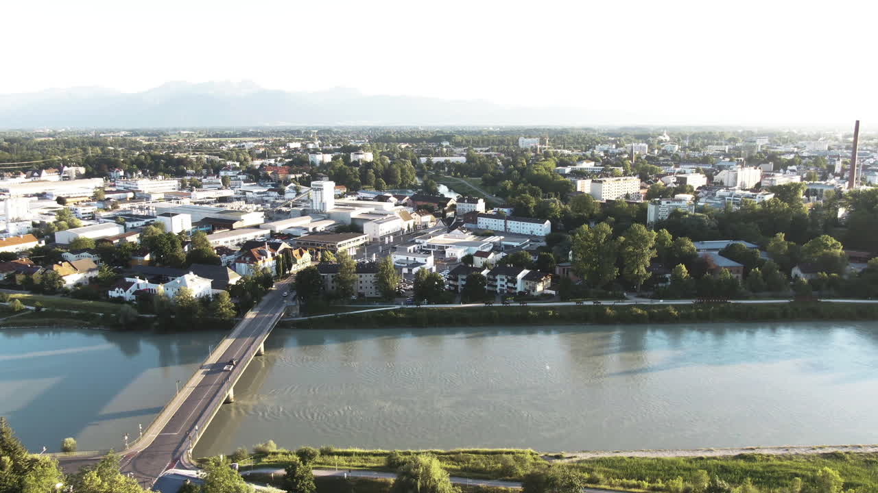 Aerial shot of cars driving over a bridge with a big skylineof a bigger city in Bavaria during sunset, there are a lot ofmountains in the distance.