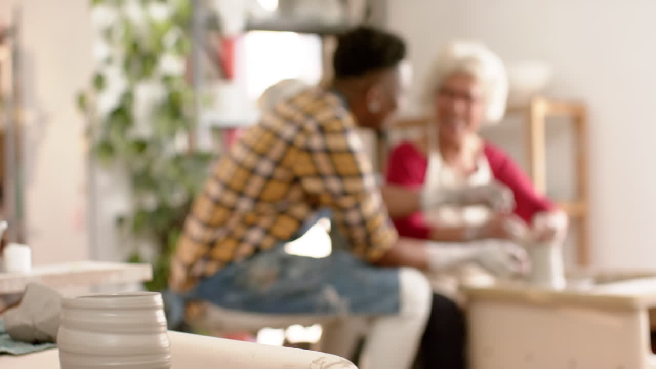 다양한 여성과 남성 도자기 제작자들이 도자기 스튜디오에서 도자기 바를 사용하여 행복합니다.