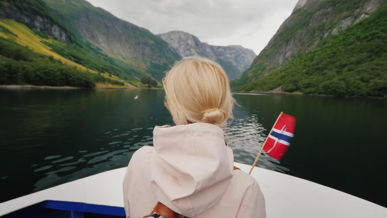 En person med et norsk flagg i hånden reiser på et skip på en pittoresk fjord.
