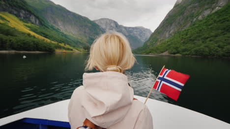 a person with a norwegian flag in his hand travels on a ship on a picturesque fjord