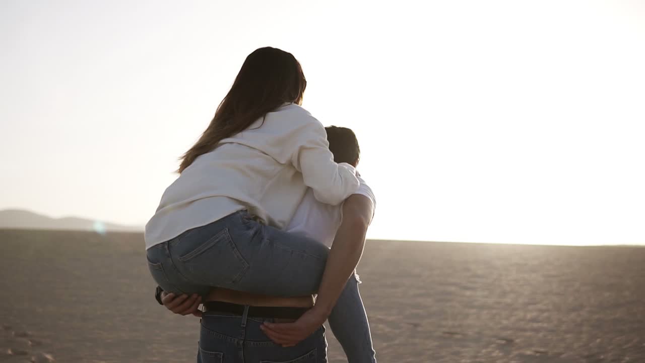 feliz y linda adorable pareja adulta en camisas blancas y vaqueros hombre con mujer novia en la espalda de cerdo, divertirse jugar, reír, sonreír en la puesta de sol en el desierto loco en el amor, las emociones y la relación. girando alrededor