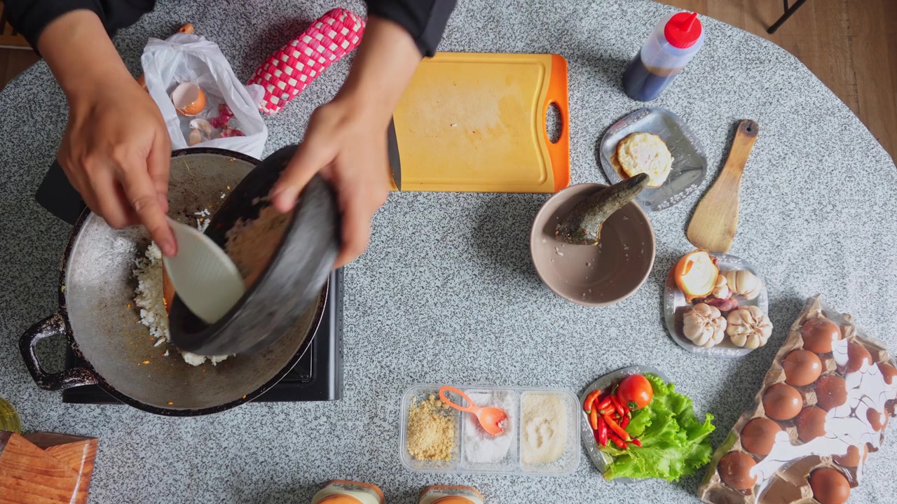 Fugleperspektiv af kok, der tilføjer dampet ris og malede aromatiske krydderier i en varm wok for at lave stegte ris