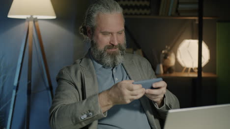 man excitedly playing a mobile game in home office at night