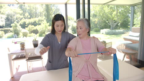 senior asian woman exercising with resistance band, guided by physiotherapist at home
