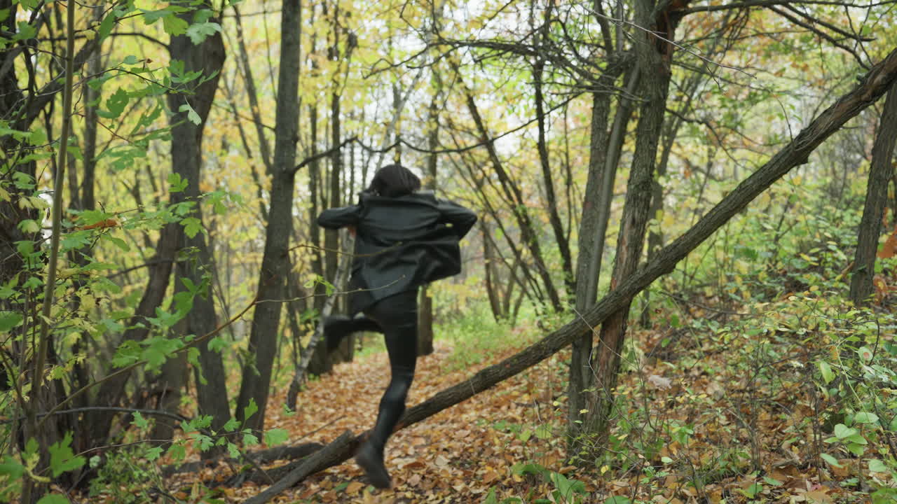 woman in leather jacket walking through forest, balancing on fallen log across leafstrewn trail, moody autumn light, solitary exploration with confident stride and rustic atmosphere