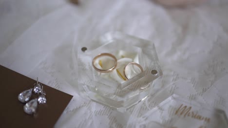 elegant close-up of wedding rings, earrings, and personalized card on lace fabric