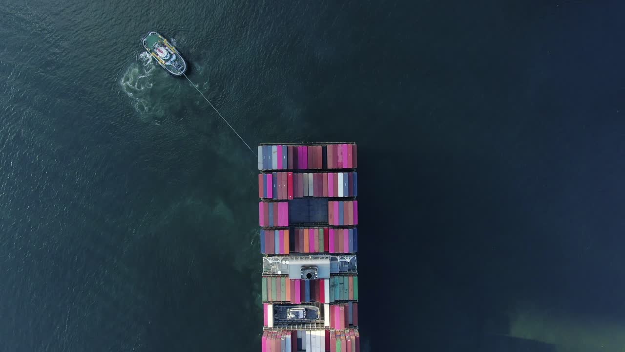 remolcador maniobrando un gran buque portacontenedores vacío en el puerto de hong kong, vista aérea