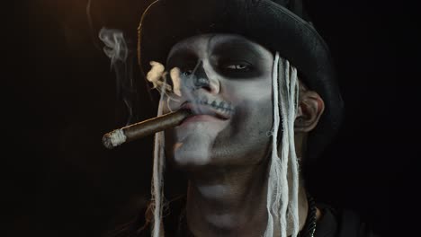 scary guy in professional carnival makeup of halloween skeleton smoking cigar, making faces, smiling