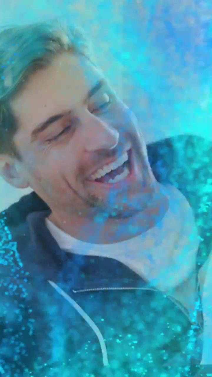 Sovrapposizione di particelle blu che fluttuano sull'obiettivo, con un uomo che ride, tiene in braccio un cane e crea un legame durante un selfie.