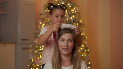 la niña le pone un sombrero de santa a su madre y la besa