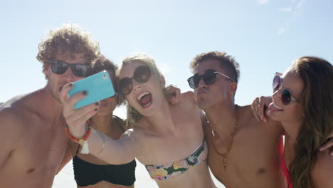 Mixed-race-group-of-friends-taking-selfies-on-the-beach-using-phone-camera