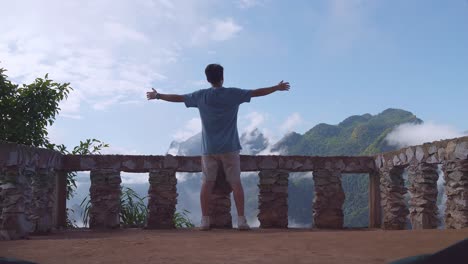 hombre excursionista asiático de pie en un acantilado de veranda y levantando las manos celebrando alcanzando la cima de la montaña nebulosa. un hombre desde la tienda vista de la montaña
