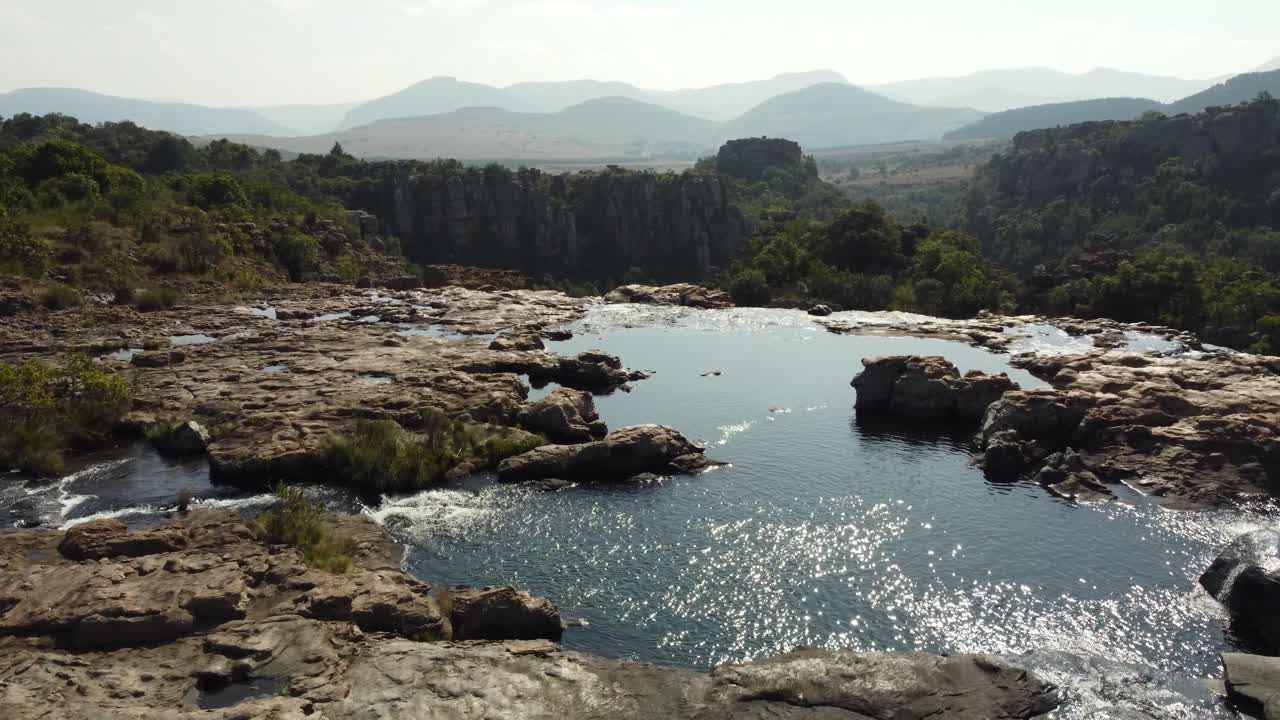 vuelo aéreo sobre piscinas de agua para revelar el paisaje del valle del bosque de drakensberg en el horizonte