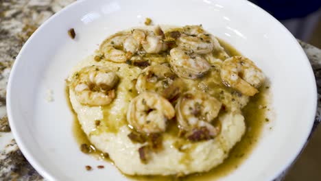 sprinkling chopped bacon on a plate of shrimp and grits