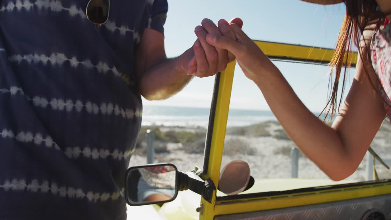 feliz pareja caucásica sentada en un buggy de playa junto al mar tomados de la mano