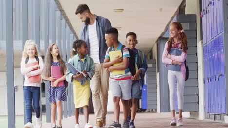 diverse male teacher and happy schoolchildren walking at school