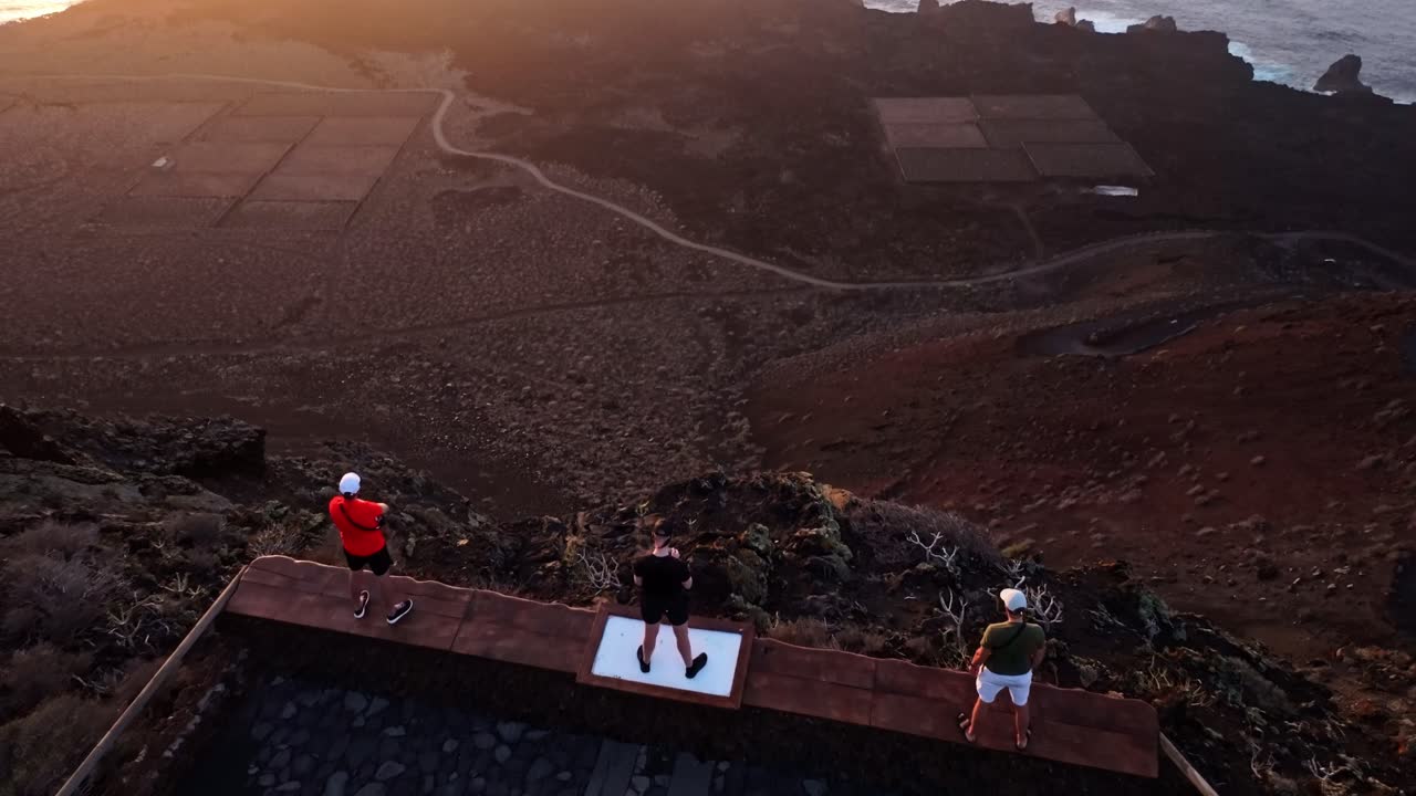 El Hierro coastline at sunset as drone glides past cliff where men stand still