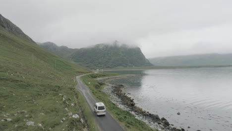 close up drone tracking shot of a campervan on a single track road during a trip of the scotland north coast 500 with a loch and cloudy topped mountains in view to passing the camper van