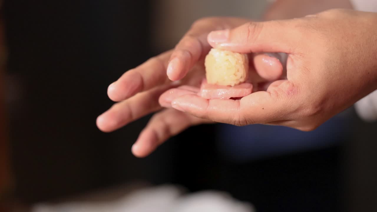 Close-up shot of a chef's hands carefully pressing rice onto raw fish for nigiri sushi