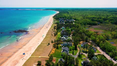 saco, maine beach packed with summer tourists in this drone aerial. crowds sunbathe, splash in ocean waves, and enjoy vacation homes lining the east coast seashore. travel paradise in full swing