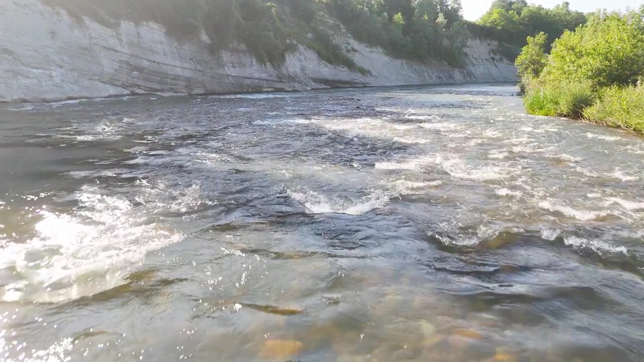 Ampia inquadratura statica di un fiume che scorre attraverso un canyon roccioso sotto la luminosa luce del sole estivo.