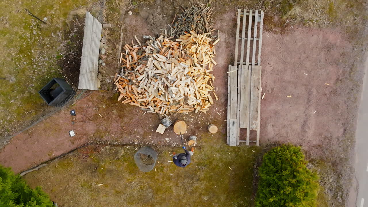 Top down drone shot rising above a man cutting firewood with an axe, spring day